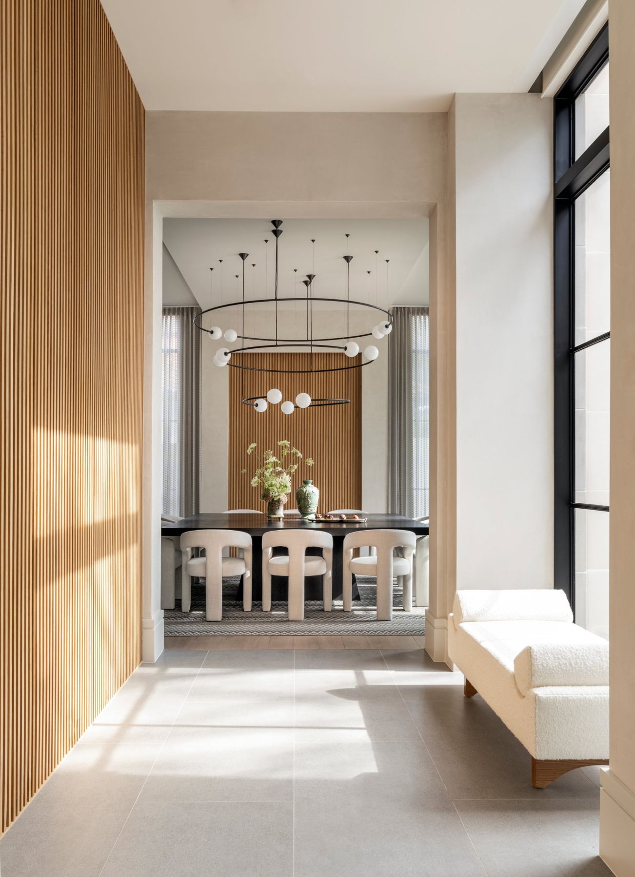 Gallery hall with a slatted oak wall leading to a dining room with a ring chandelier