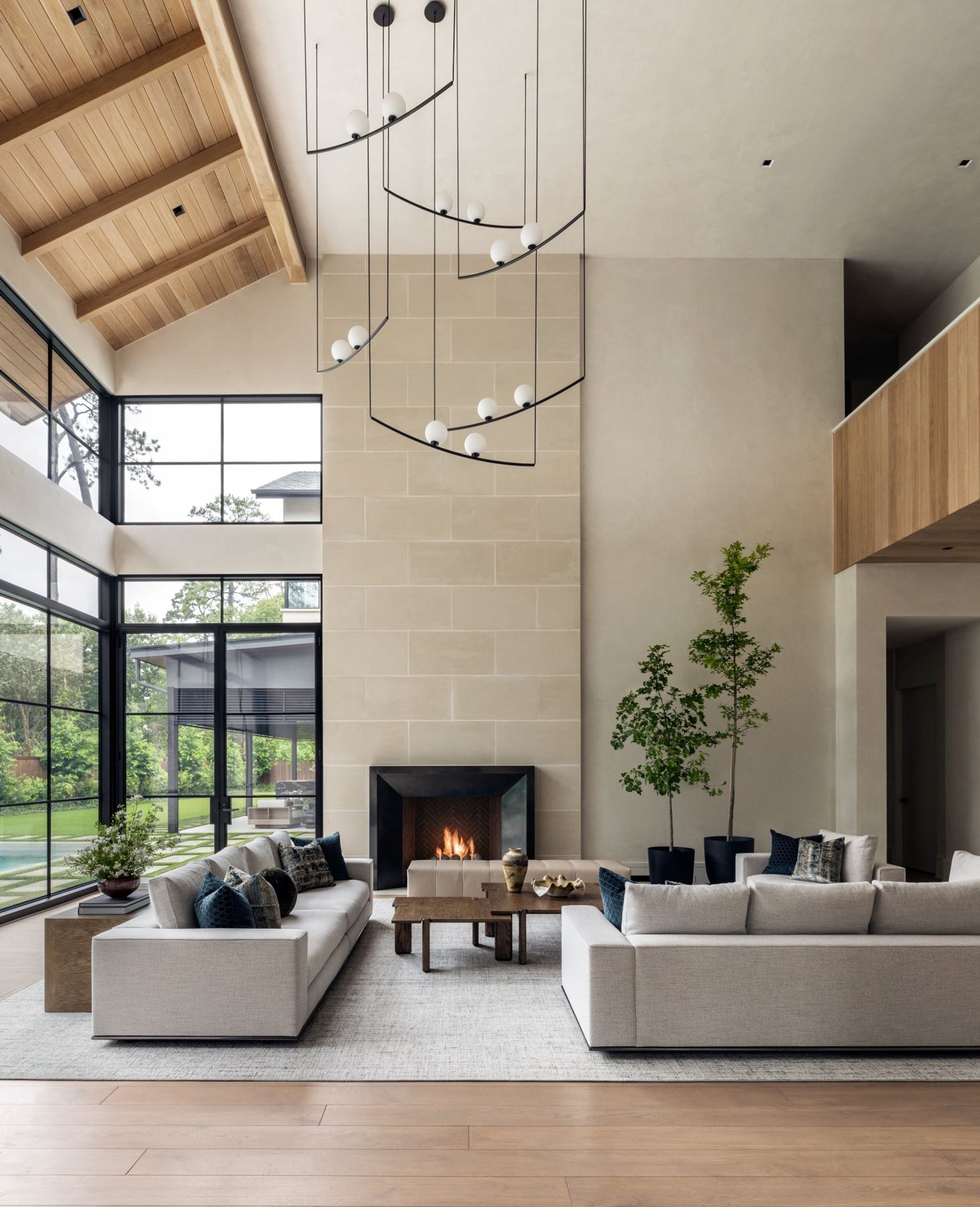 Two-story great room with a vaulted oak ceiling, sculptural globe pendants and steel windows onto the pool