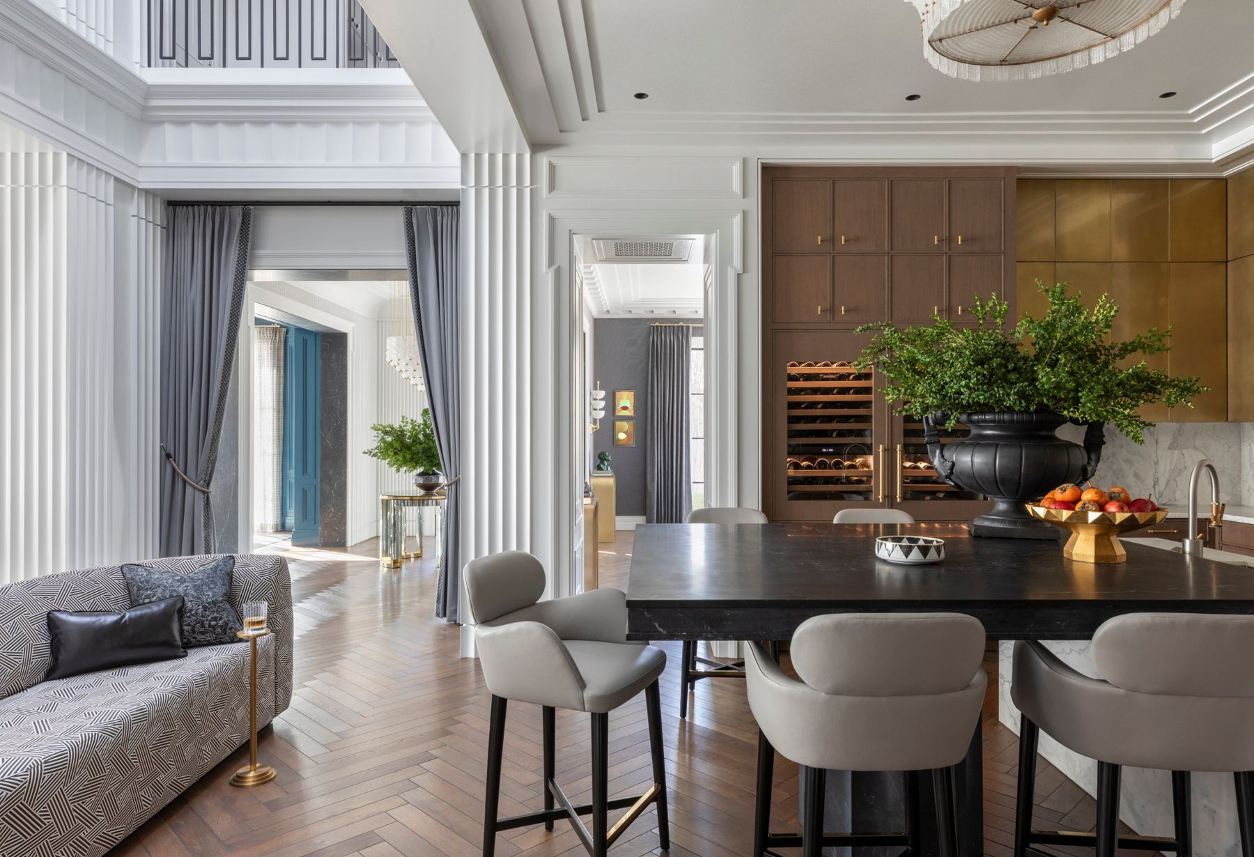 Kitchen island beneath fluted white columns, with brass and walnut cabinetry and a lit wine wall