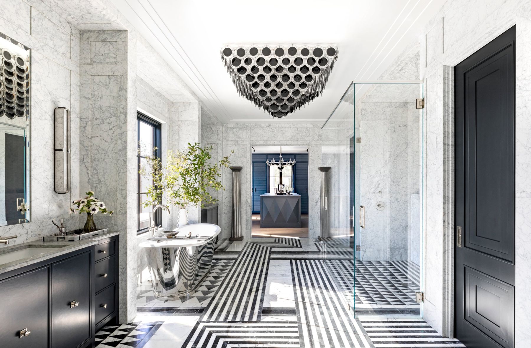Marble primary bath with a striped black and white floor, polished nickel tub and a glass disc chandelier