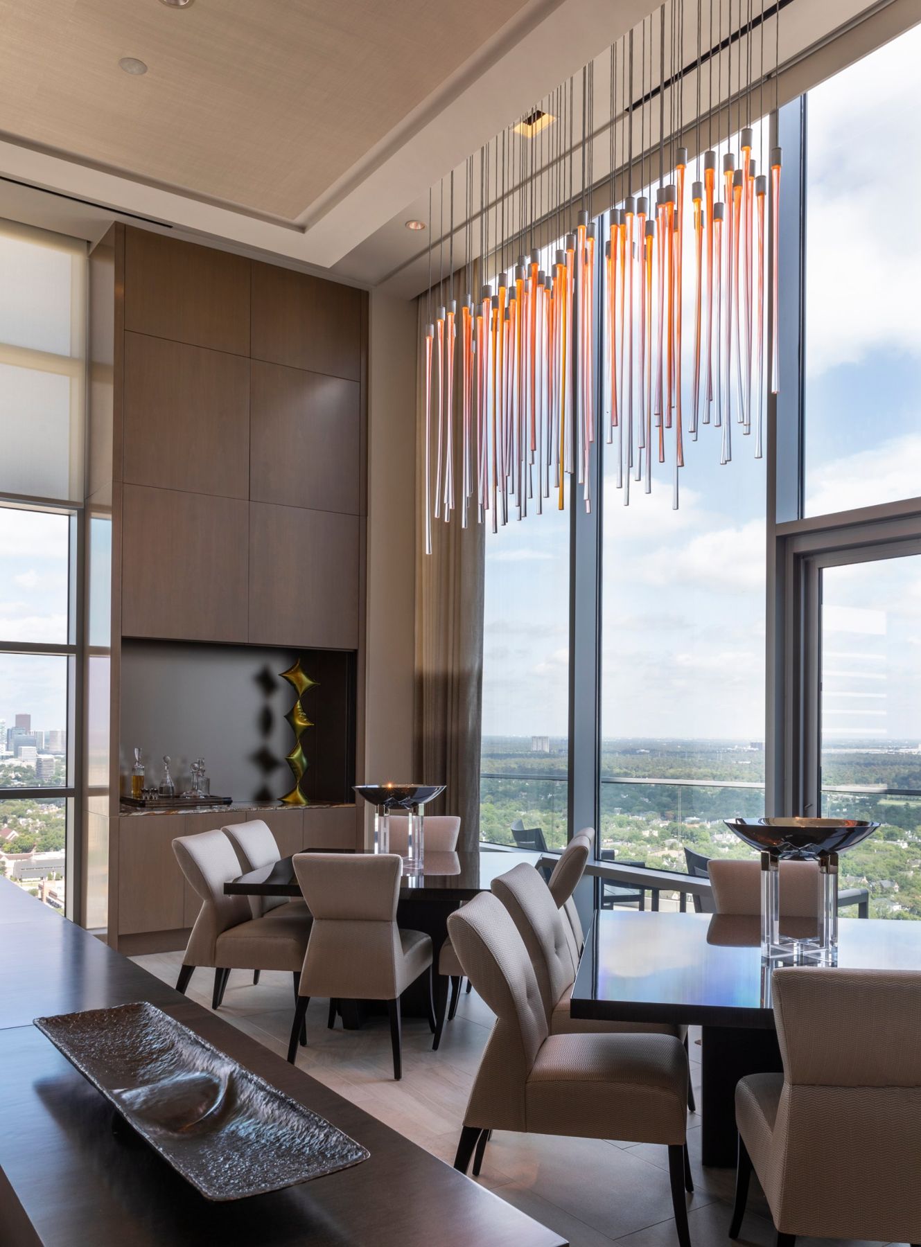 Dining room under a cascading amber glass chandelier with double-height windows onto the city