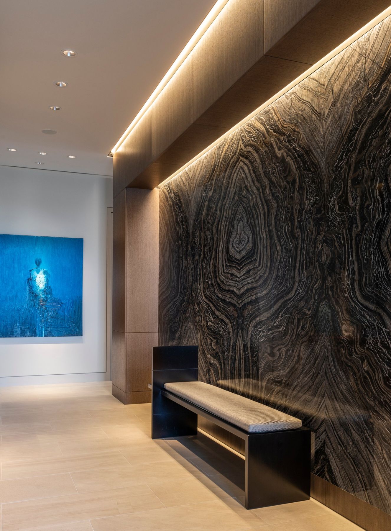 Entry gallery with a book-matched stone wall washed by a concealed light cove