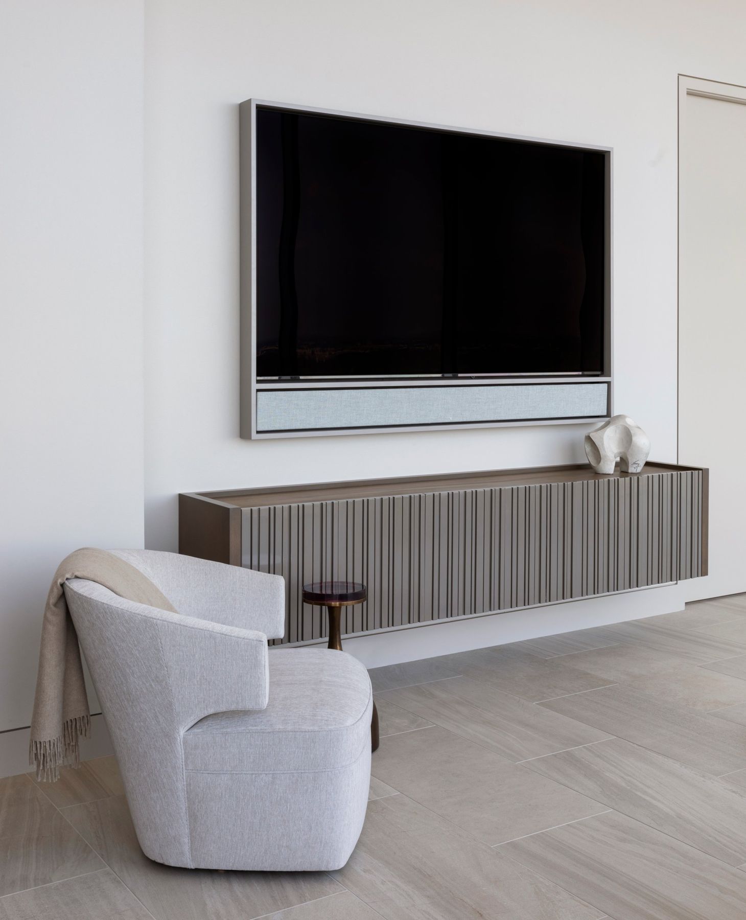 Framed TV with a fabric-covered sound bar above a floating fluted cabinet