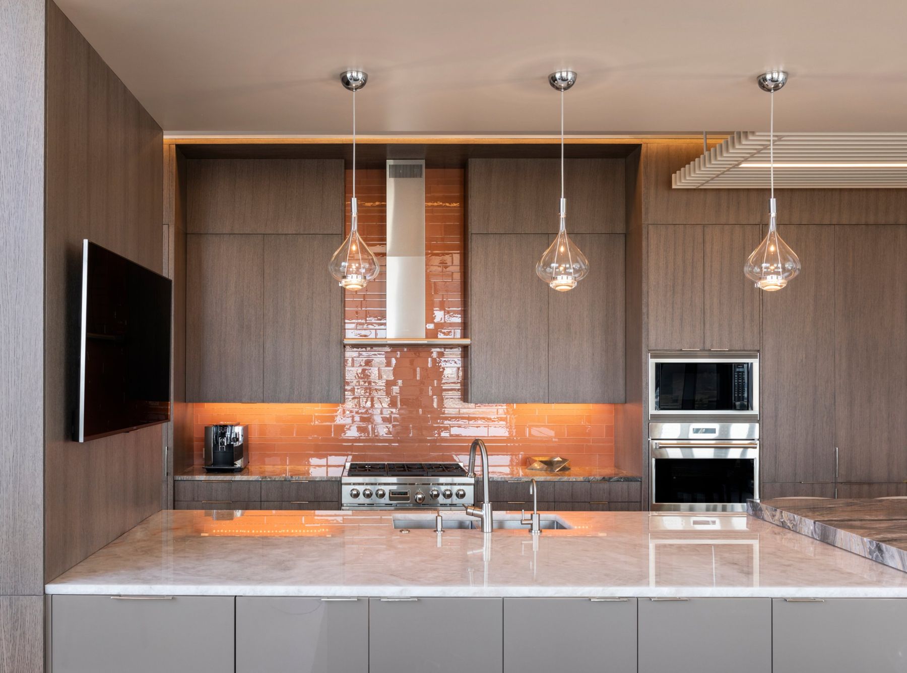 Walnut kitchen with a glossy amber tile backsplash, glass pendants and a wall-mounted TV