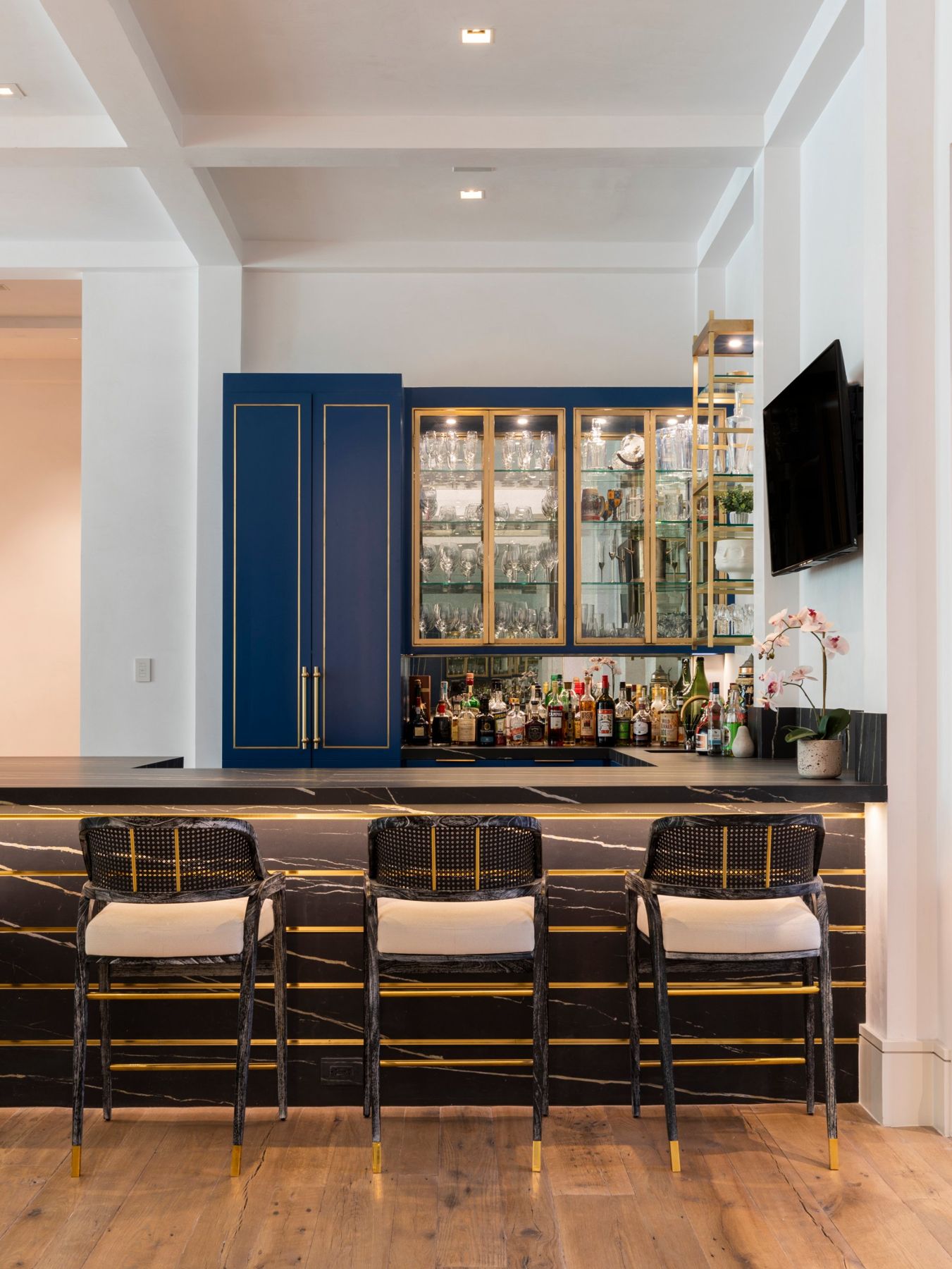Blue and brass bar with lit glass cabinets and a black stone counter with brass inlays