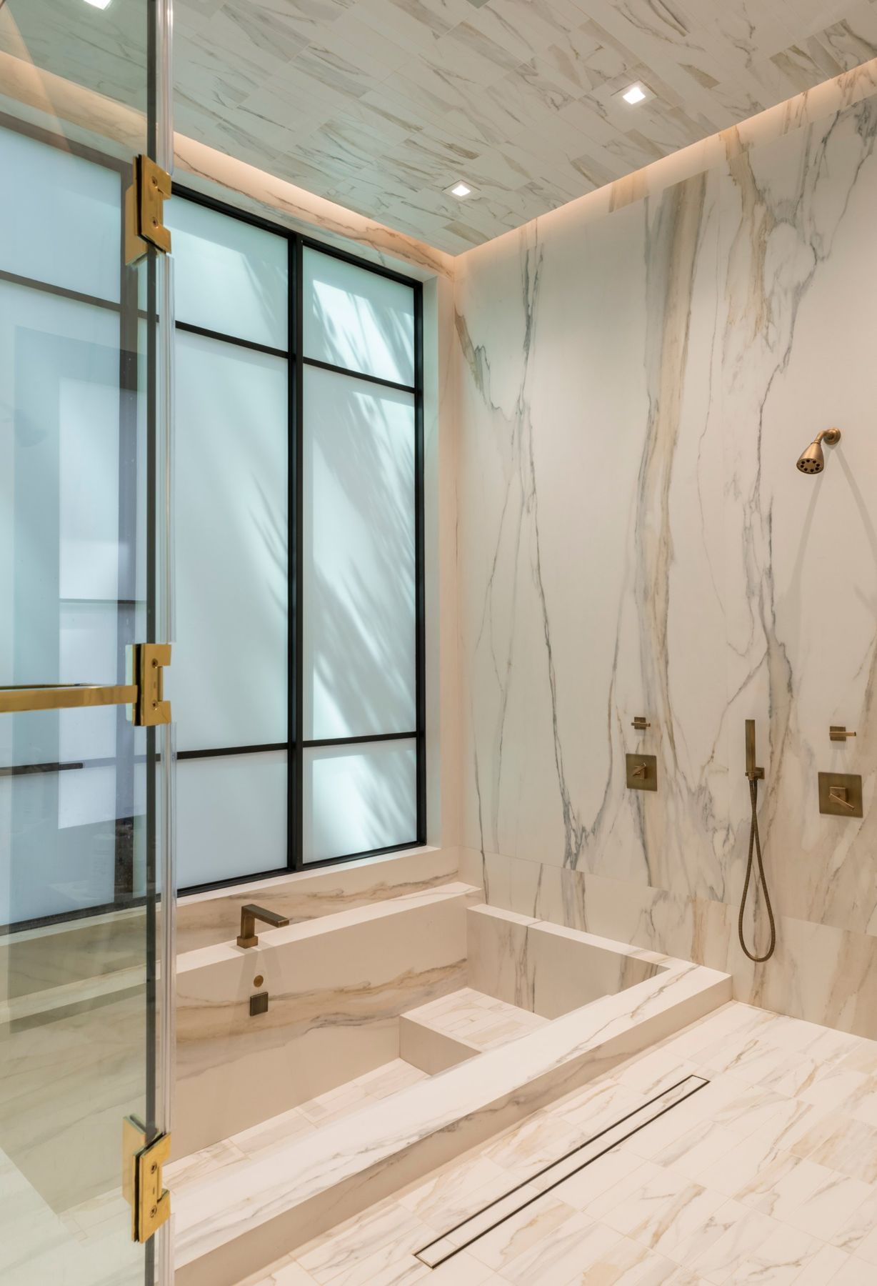 Stone wet room with a sunken tub beneath a tall steel-framed window