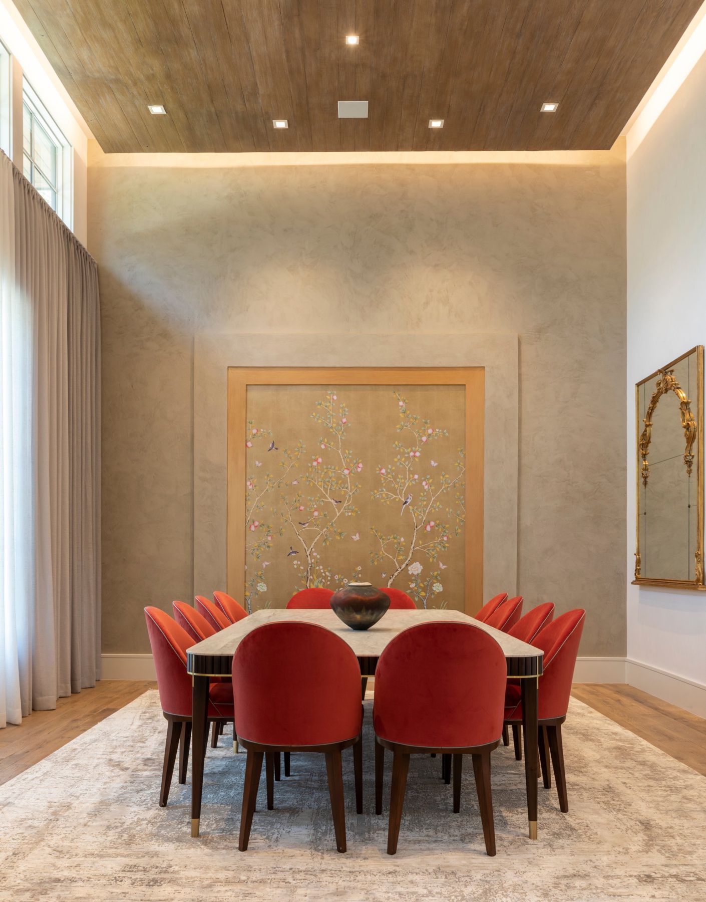 Dining room with red velvet chairs, a gilded chinoiserie panel and a wood ceiling edged with cove light