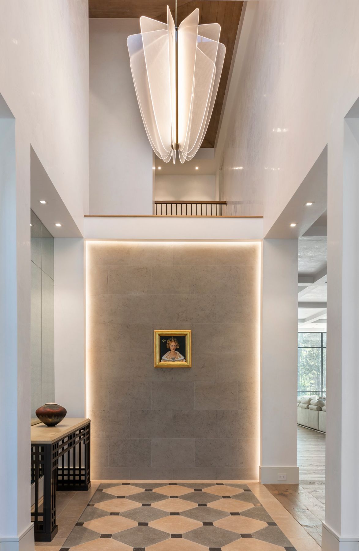 Two-story entry with a sculptural acrylic pendant and a stone wall framed by a light cove