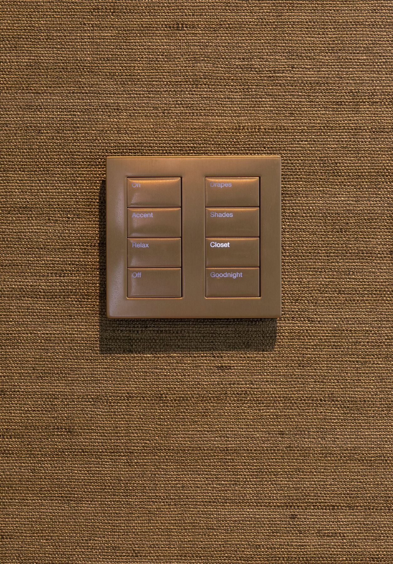 Bronze keypad on grasscloth with buttons for On, Accent, Relax, Off, Drapes, Shades, Closet and Goodnight