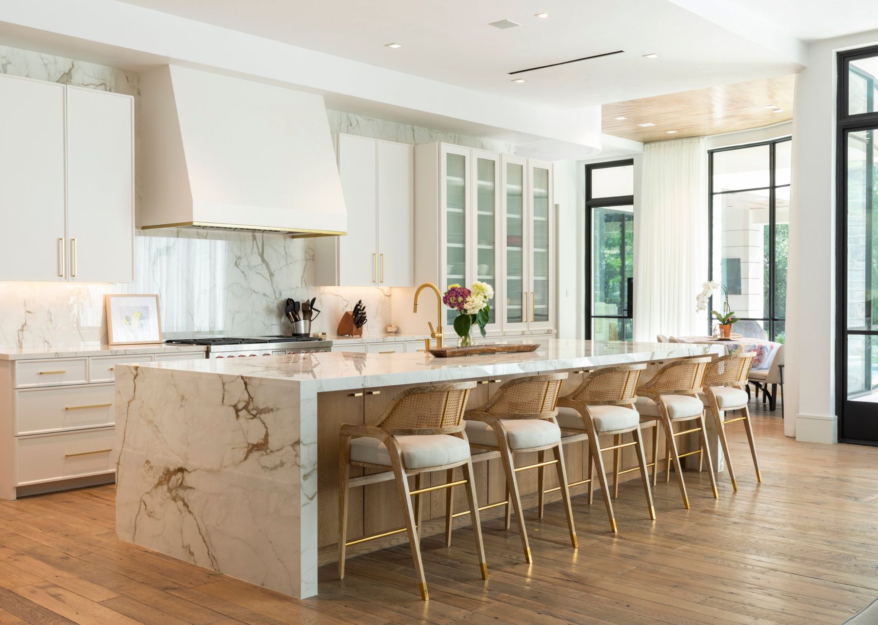 White kitchen with a marble waterfall island, brass hardware and cane counter stools