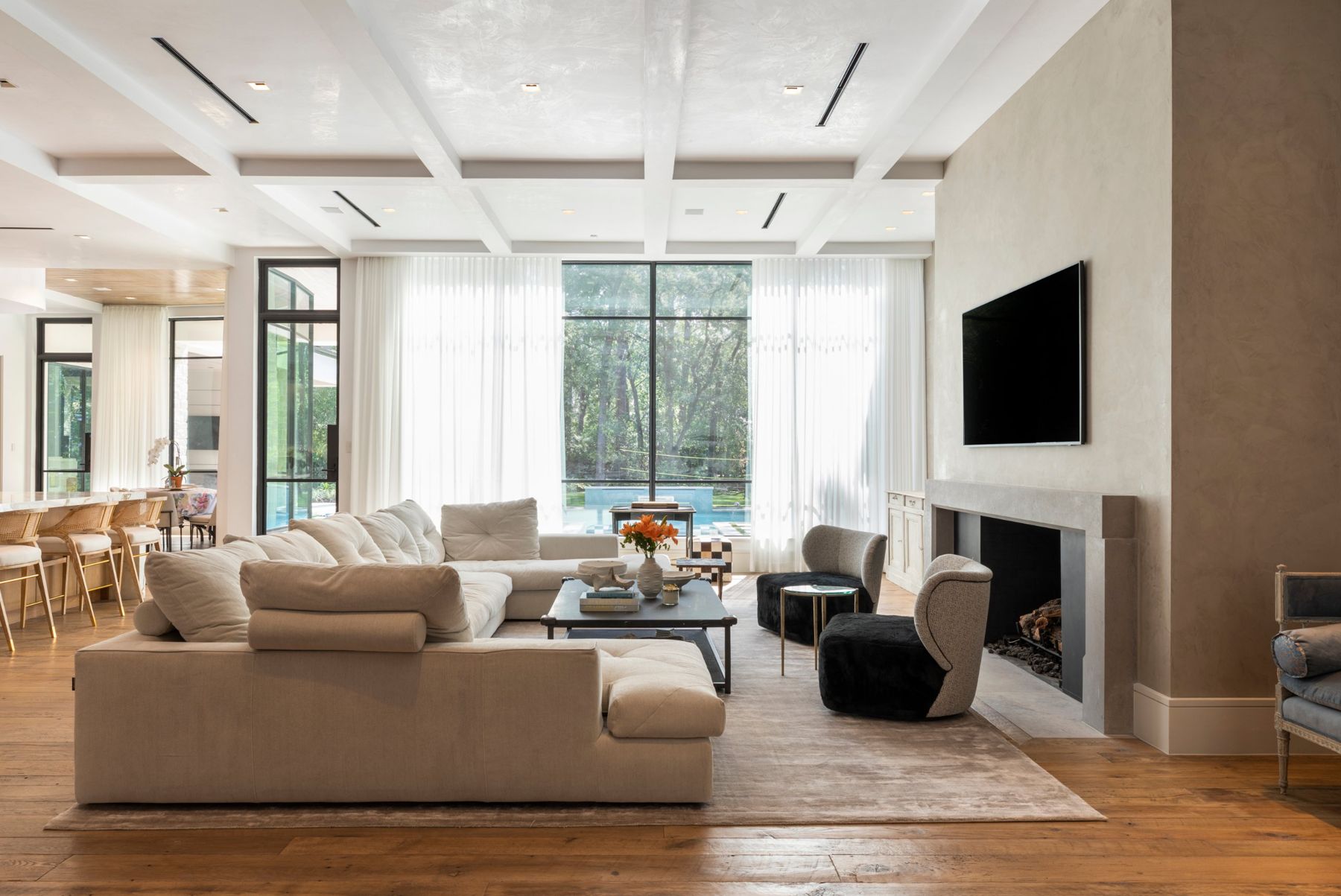Family room with a coffered ceiling, sheer drapery over tall steel windows, a wall-mounted TV and a plaster fireplace wall
