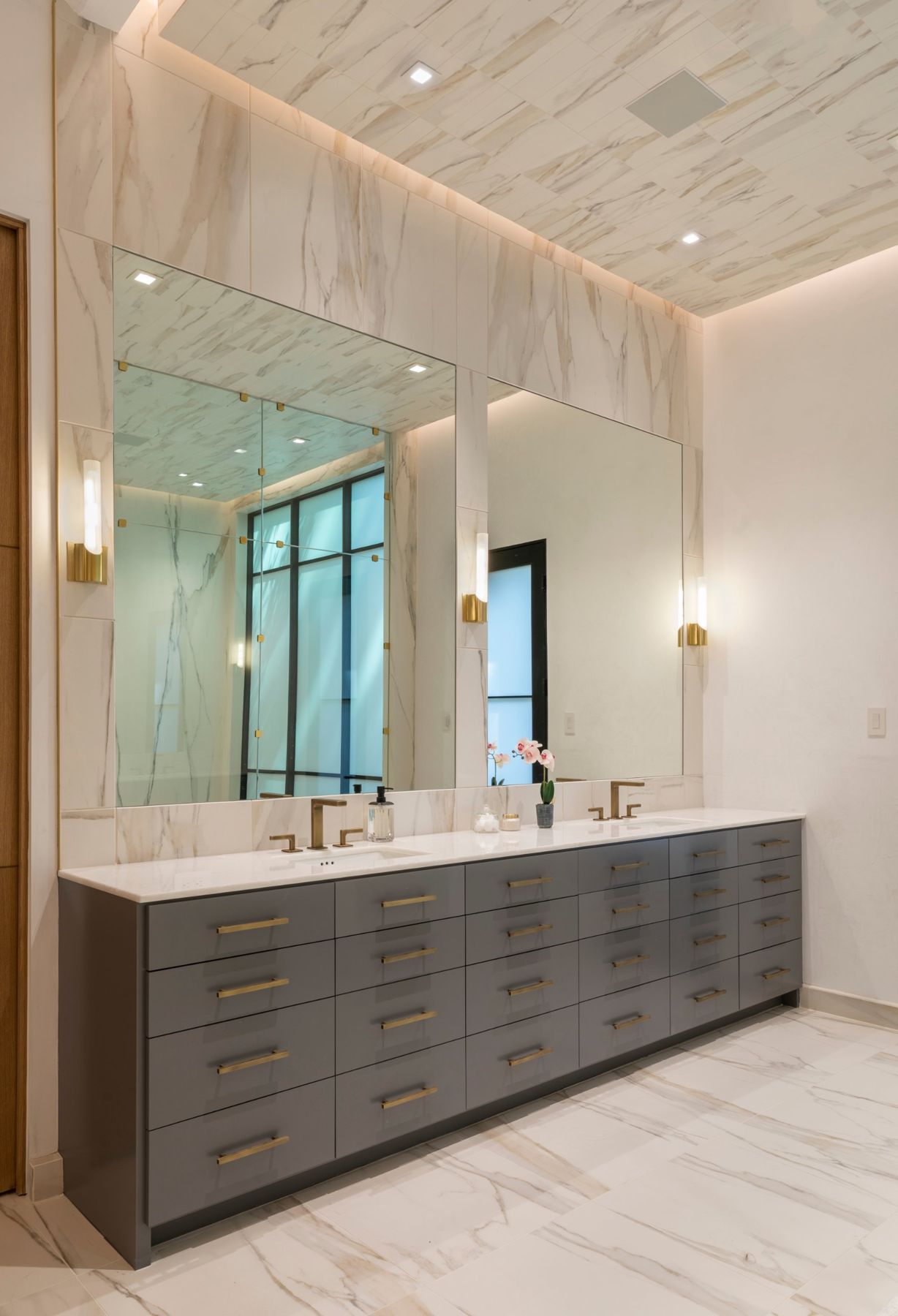 Primary bath vanity with brass sconces, large mirrors and a stone ceiling edged in light