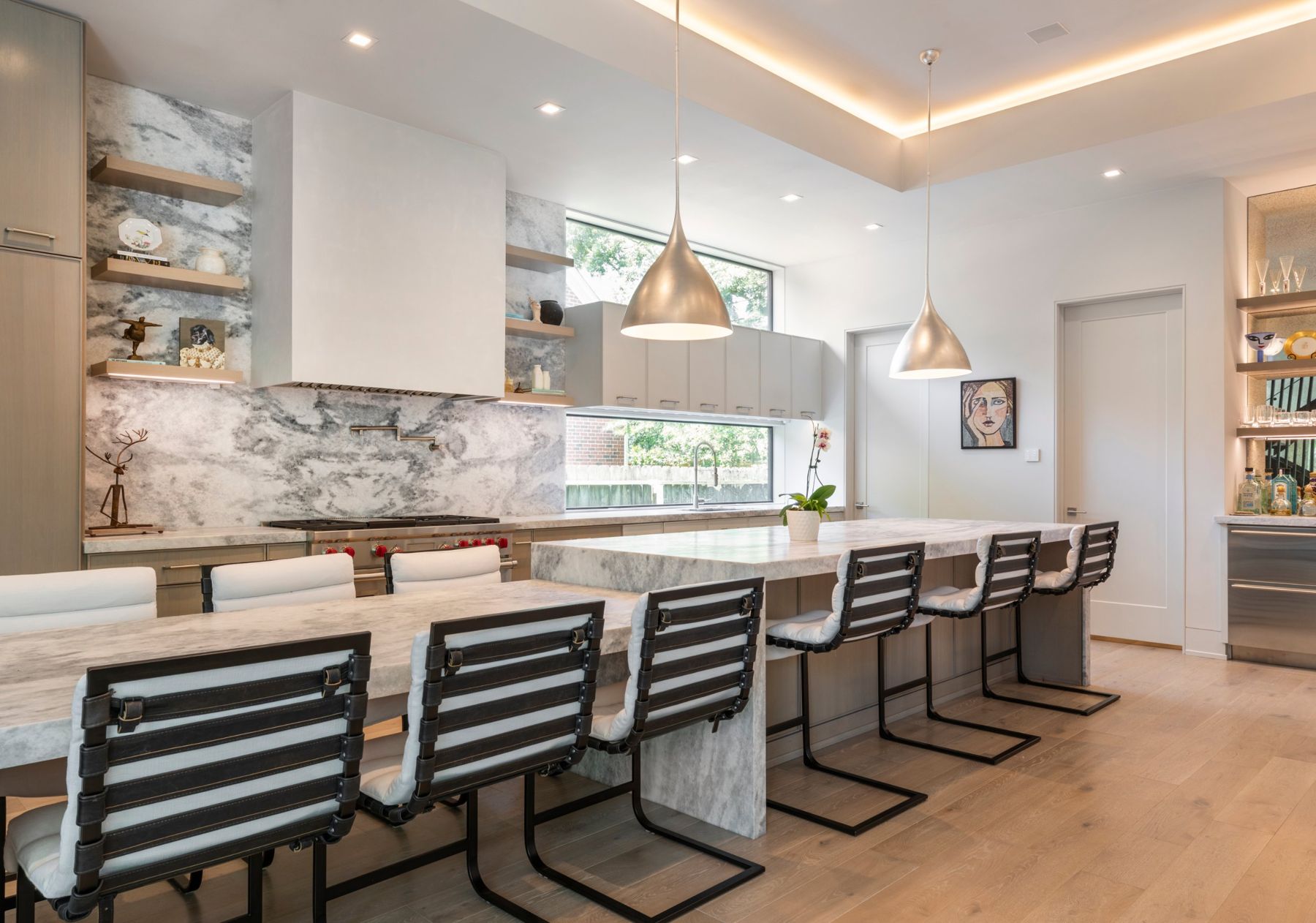 Kitchen with a long quartzite island, cove lighting and silver pendants