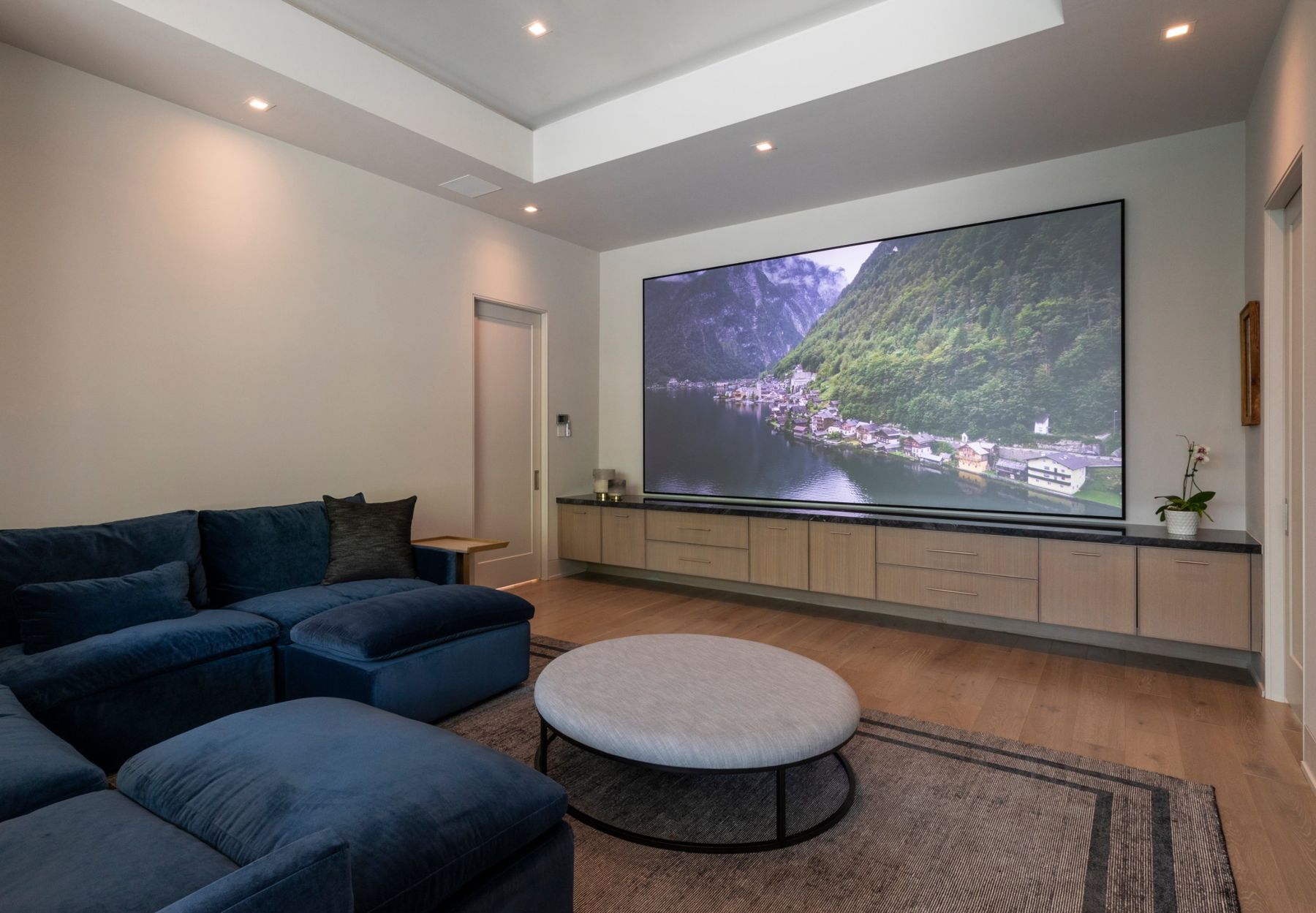 Media room with a large screen above floating oak cabinetry and a blue velvet sectional