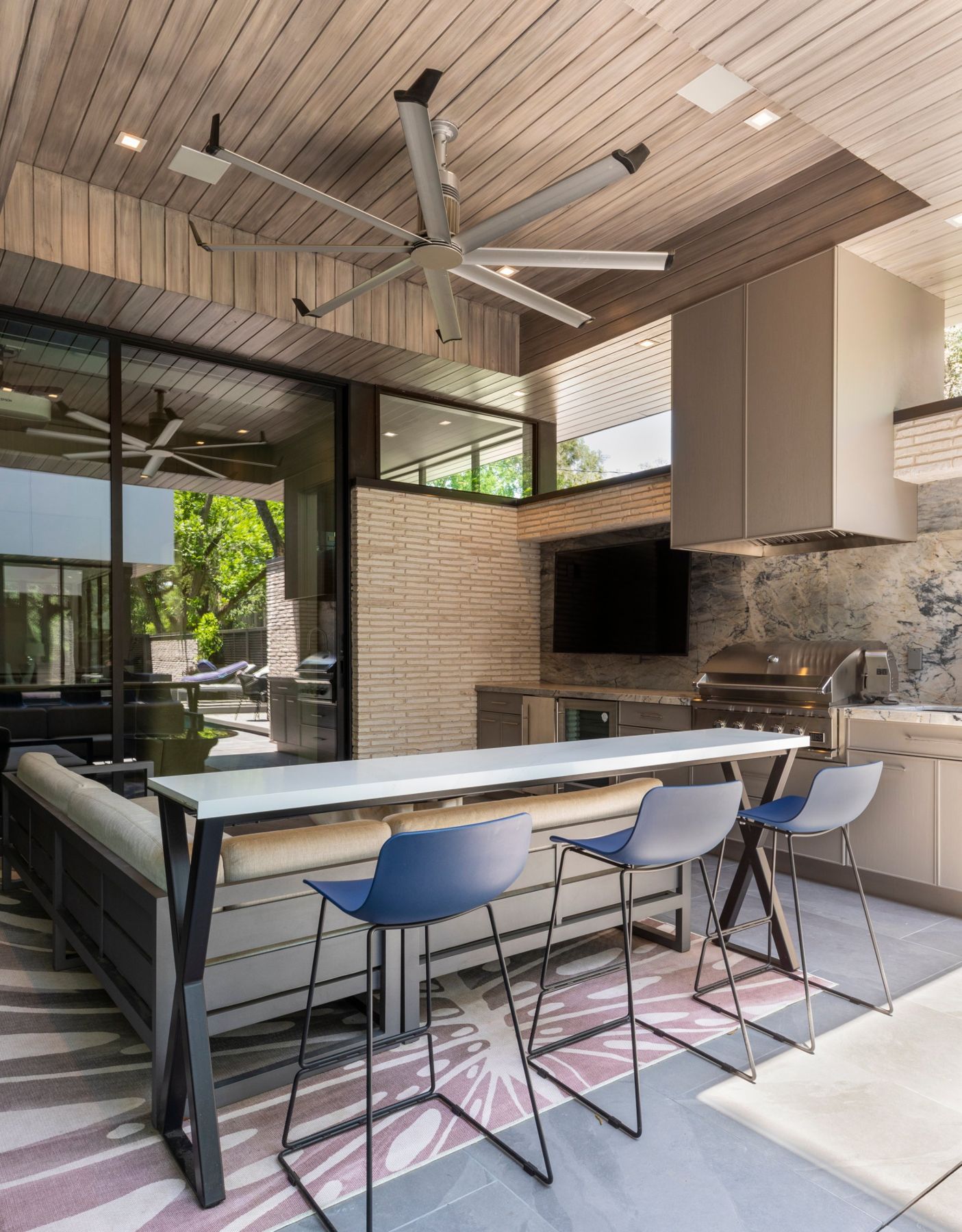 Covered outdoor kitchen and bar with an outdoor TV, ceiling speakers and a large fan