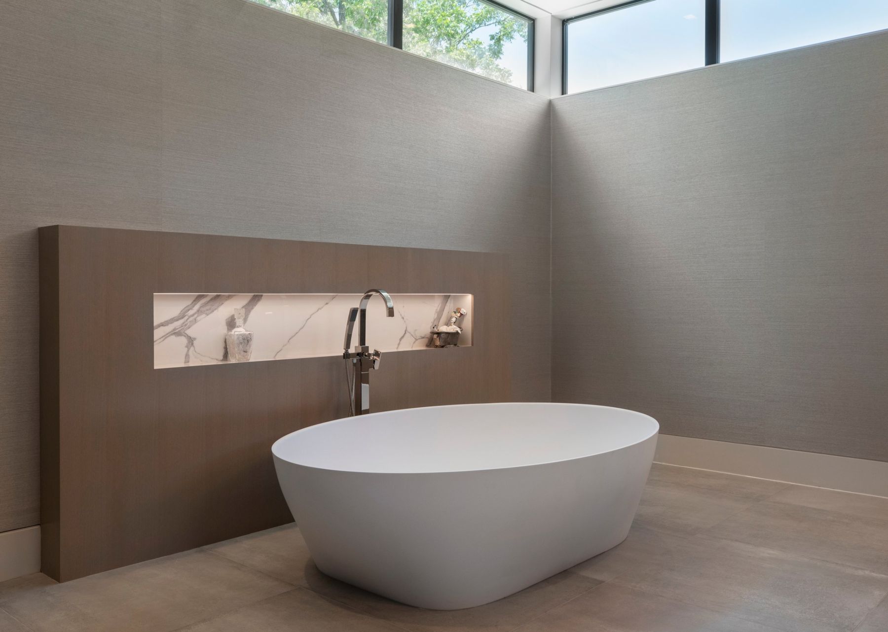Freestanding tub in front of a lit stone niche under clerestory windows