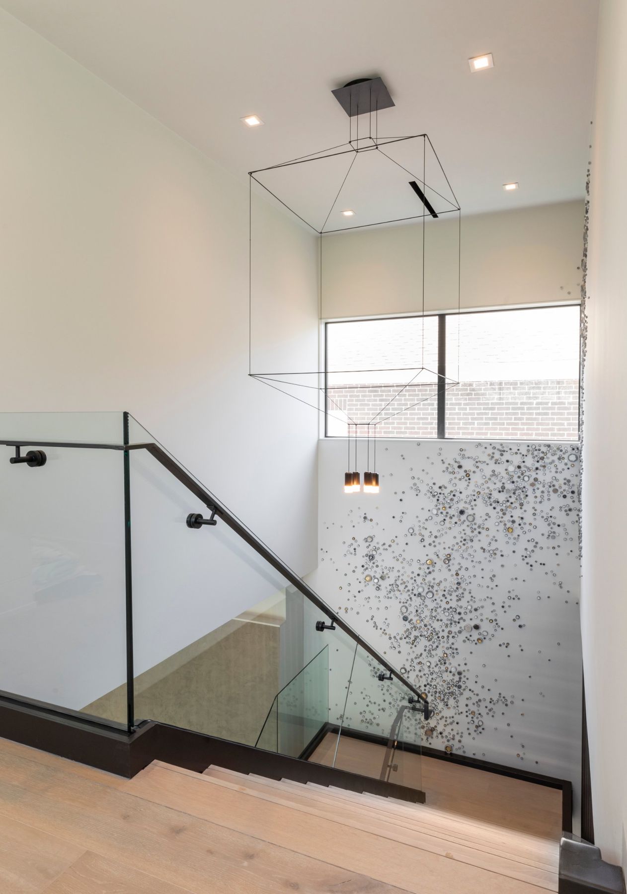 Stairwell with a glass rail, a wire-frame pendant and a scattered glass art installation
