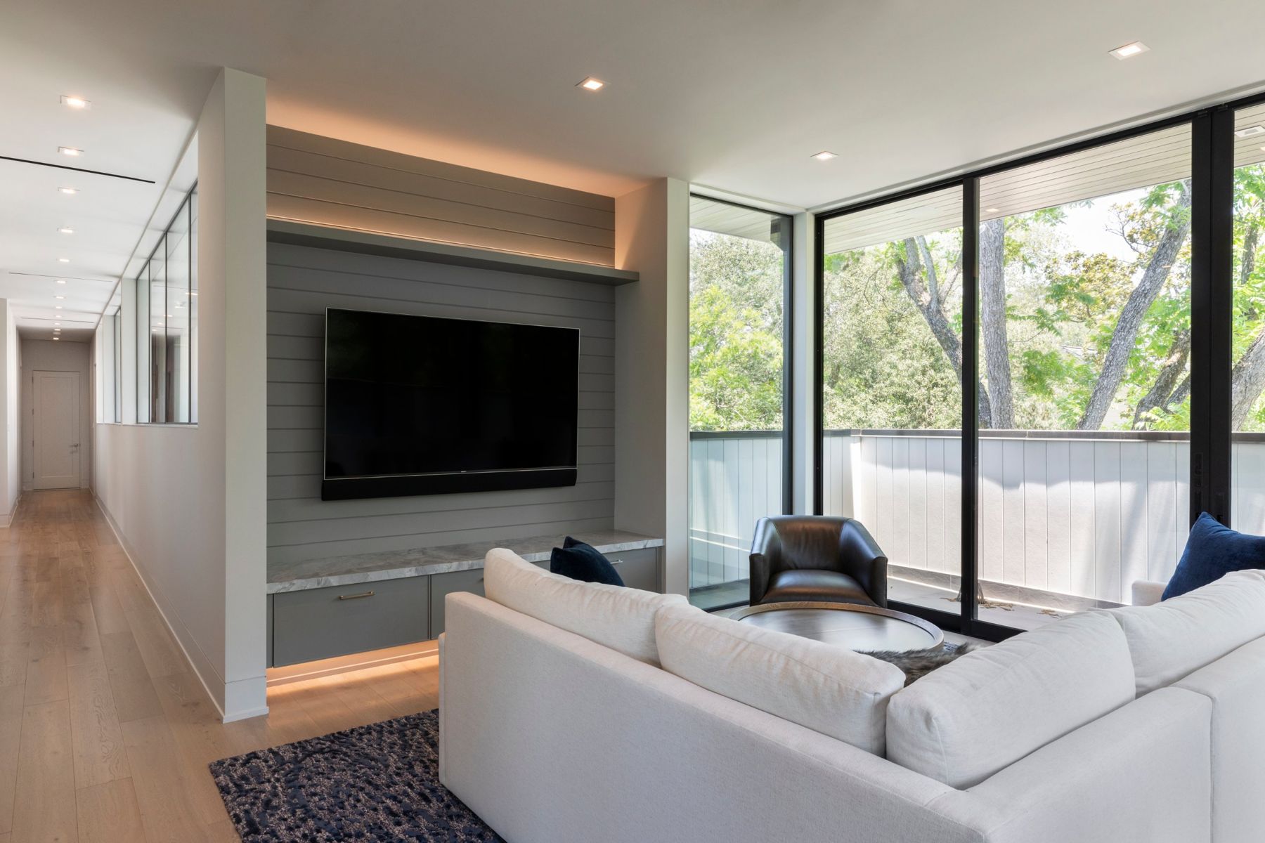 Upstairs lounge with a TV on a lit shiplap wall and floor-to-ceiling glass onto the trees